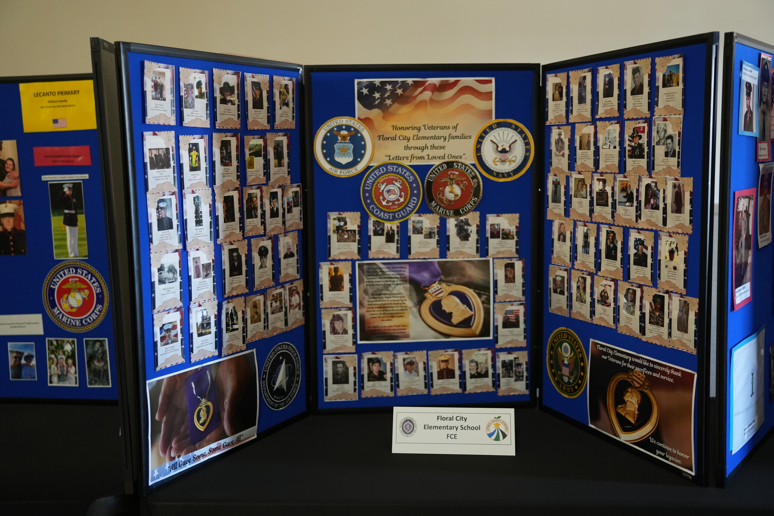 A multi-panel display board honors veterans with photographs, military seals, and text.